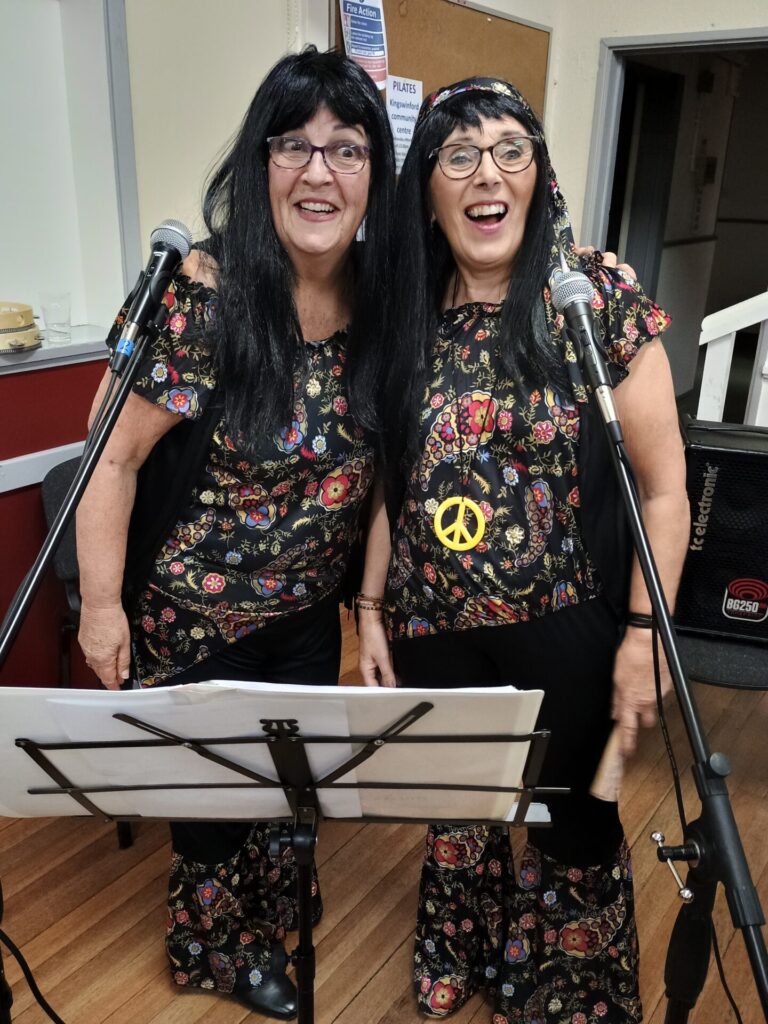 Two ladies in matching outfits and wigs leading the singing
